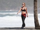 De barriga de fora, Adriana Esteves caminha em praia carioca