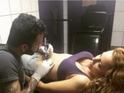 Aos 43 anos, Rita Guedes posa com a barriguinha de fora fazendo tatuagens